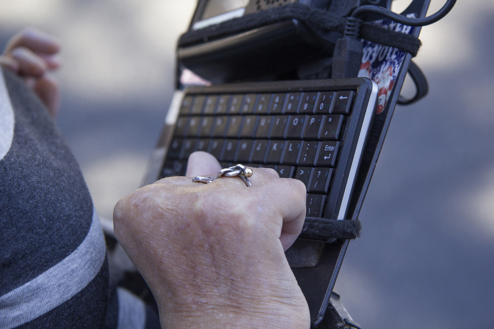Photo of a hand with folded fingers in front of a keyboard attached to a wheelchair.